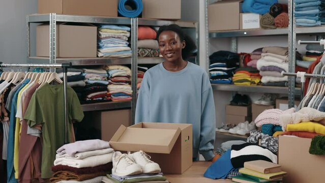 Portrait view of the multiracial happy woman looking at the camera with wide smile while working at the center of reuse clothes. Second hand and sustainability concept
