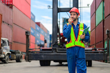 Smiling portrait of smart male industrial engineer worker with hard hat and safety vest at cargo...