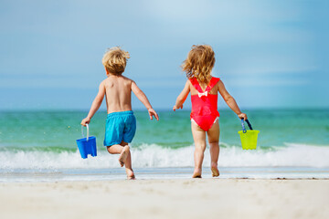 Naklejka premium View from behind of a boy and girl run with bucket to ocean