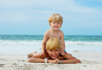 Two happy smiling boys lay together on sand ocean sea beach