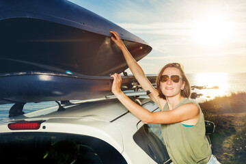 Woman in sunglasses unload car roof top baggage at sea parking