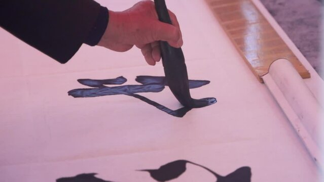 Person's Hand Writing Chinese Calligraphy On Paper With Ink Brush. closeup