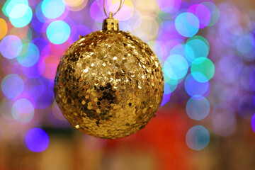 Christmas toy, golden shiny ball hanging on blurred festive lights background. New Year decorations