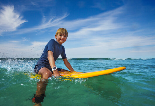 Teen boy sit on orange surfboard in ocean waiting wave
