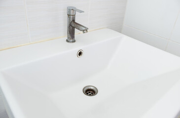 The ceramic sink basin with the stained faucet near the white tile wall.