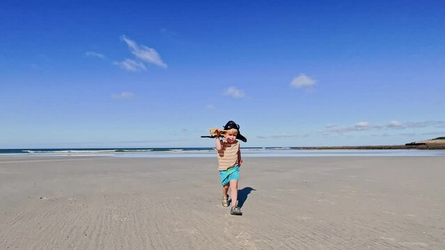 Little blond boy in aviator hat run with toy plane on beach