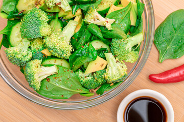 Fresh Green Salad of Avocado, Broccoli, Spinach and Cucumber with Soy Sauce and Red Hot Pepper on Wooden Cutting Board. Vegan Salad. Vegetarian Culture. Raw Food. Healthy Eating and Vegetable Diet
