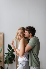 Cheerful man hugging positive girlfriend in pajama at home.