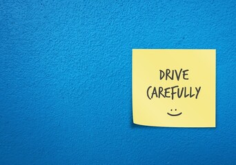 Bright blue wall copy space background with yellow note written with smiley DRIVE CAREFULLY ,...