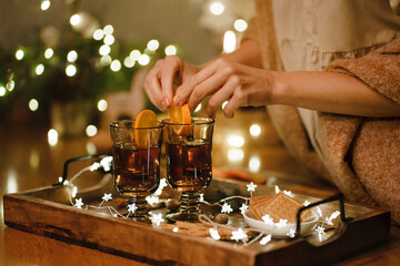 Female hands hold cup of tea next to cookies and Christmas tree on tray. Selective focus.