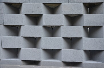 a concrete block fence encloses the yard. a robbing perennial bed in the foreground of a dark gray wall. holes inside the wall in the grid. The checkerboard pattern is an ornamental detail like a slot