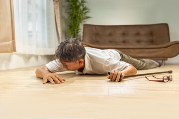 Asian senior man falling down and lying on the floor while walk with walking stick at home.