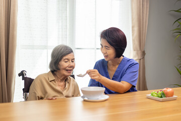 Caregiver feeding elderly asian woman with soup.