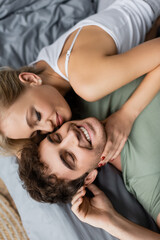 Top view of young woman in pajama touching neck of positive boyfriend on bed.