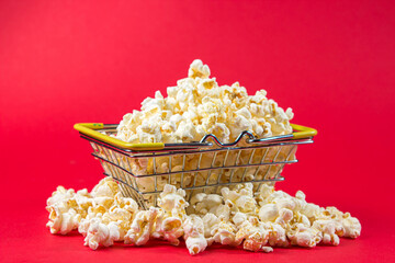 Popcorn in a small shopping basket on a red background.