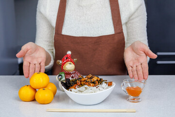 The girl holds a plate of rice noodles and chicken in her hands. Tangerines on the table. Dark home kitchen background