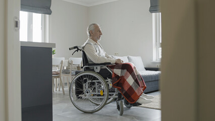 Fototapeta na wymiar Senior man in wheelchair feeling sad at home, living alone at senior age