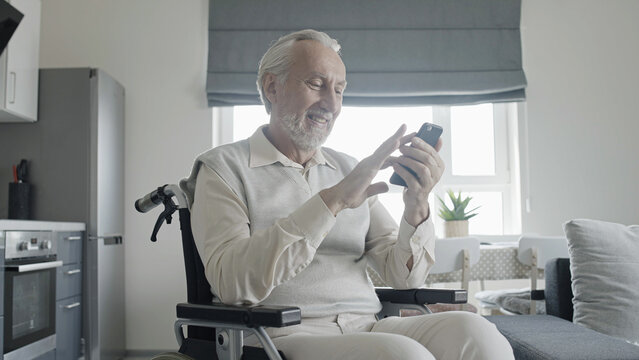 Happy senior man with disability scrolling photos in smartphone app, social media, internet