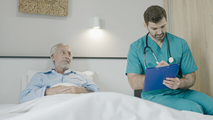 Obraz premium Doctor talking to senior patient in bed, writing down in patient's card, elderly care