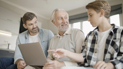 Obraz premium Grandfather, father and son spending time together, discussing game on laptop, three family generations 