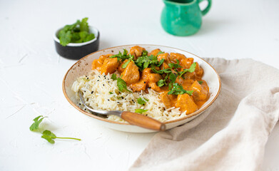 Traditional Indian dish chicken curry with basmati rice and fresh cilantro on rustic white plate on white concrete kitchen table, close up with selective focus. Indian dinner meal