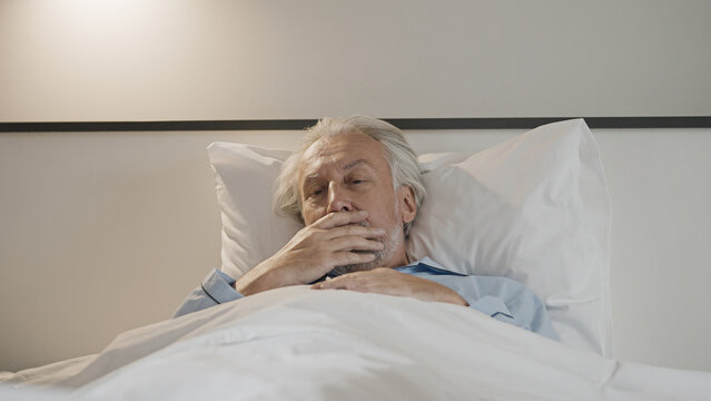 Sick Elderly Man Lying In Bed, Feeling Nausea Or Coughing, Suffering From Disease