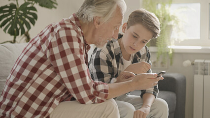 Teen boy teaching grandfather how to use smartphone, family support and care