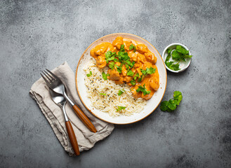Traditional Indian dish chicken curry with basmati rice and fresh cilantro on rustic white plate on gray concrete table background from above. Indian dinner meal