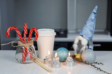 A glass of coffee, chopsticks, a Christmas figurine and candies on a white table against a dark kitchen background