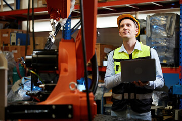 Fototapeta premium factory worker or engineer holding a laptop computer and controlling robot machine in the factory