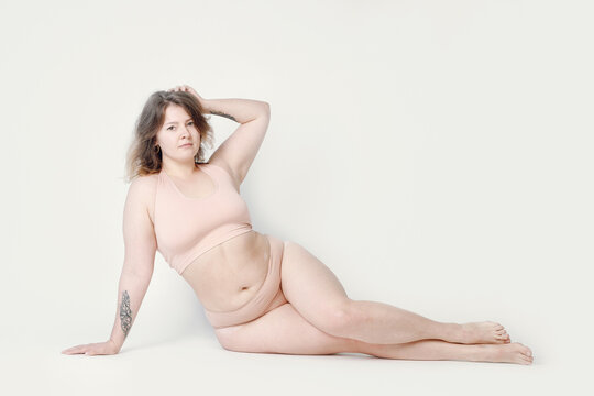 A large woman in underwear lying on the floor on a light background. Plump girl plus size, positive attitude to the body.