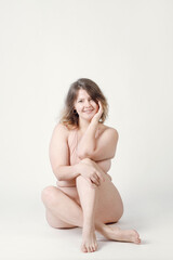 Obraz premium A plump woman with a hairstyle, smiling at the camera, sitting in the studio in her underwear. A bodypositive large-sized woman who feels comfortable in her natural body.