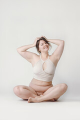 Obraz premium A plump woman with a hairstyle, smiling at the camera, sitting in the studio in her underwear. A bodypositive large-sized woman who feels comfortable in her natural body.
