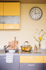 yellow grey kitchen interior with clock on beige wall fruits and flower, compact kitchen gallery in yellow and gray colors, Scandinavian kitchen interior, household cooking routine, simple mock up