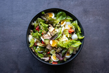 Salad bowl with vegetables, chicken and eggs. Dark background. 