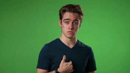 Confused young man 20s posing isolated on green screen background in studio. People lifestyle concept. Pointing fingers himself ask say who me waving and smiling