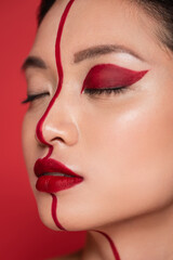 close up portrait of asian woman with closed eyes and creative visage on face divided with line isolated on red.