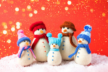 Family of knitted snowmen celebrate the holidays on a red background with golden lights. Winter...