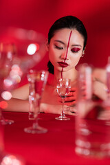 young asian woman with red artistic visage looking at glass with pure water on blurred foreground.