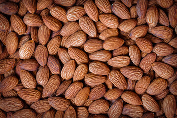 Almonds all over close-up. Brown fresh or roasted almond kernels top view, food background