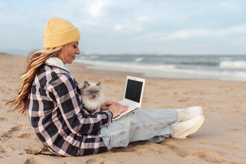 nomad woman using laptop computer on a beach sitting with her cat. Freelance work concept
