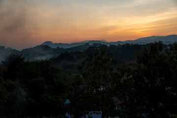 Fototapeta na wymiar orangener goldener Sonnenuntergang in Chiang Rai, Norden von Thailand mit Bergen im Hintergrund, hinter welche die Sonne verschwindet