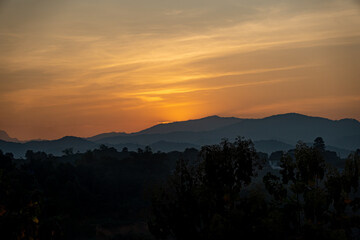 orangener goldener Sonnenuntergang in Chiang Rai, Norden von Thailand mit Bergen im Hintergrund, hinter welche die Sonne verschwindet