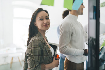 Obraz premium Young female designer standing in office near colleagues working on glass wall