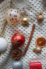 Various colorful Christmas ornaments, small presents and seasonal spices on white knitted blanket. Top view.