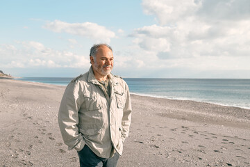 Happy middle-aged bearded man walking along deserted winter beach. Concept of leisure activities, wellness, freedom, tourism, healthy lifestyle and nature.