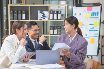 Team business three smiling and happy Asian men and women team using tablets and laptops brainstorm and plot statistics on a corporate chart board inside the company. Colleagues concept.