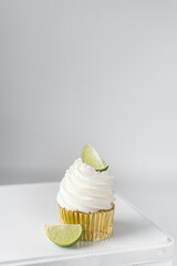 Lime cupcake on a white metal tin, lime cupcake with white buttercream and a a lime wedge,...