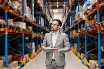 A warehouse manager is using tablet for tracking goods while standing in warehouse.