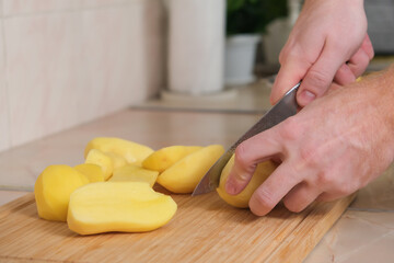 A man cuts potatoes in half with a knife to use a food processor. Preparation of potatoes for cooking. A man cooks dinner or lunch at home for the family.